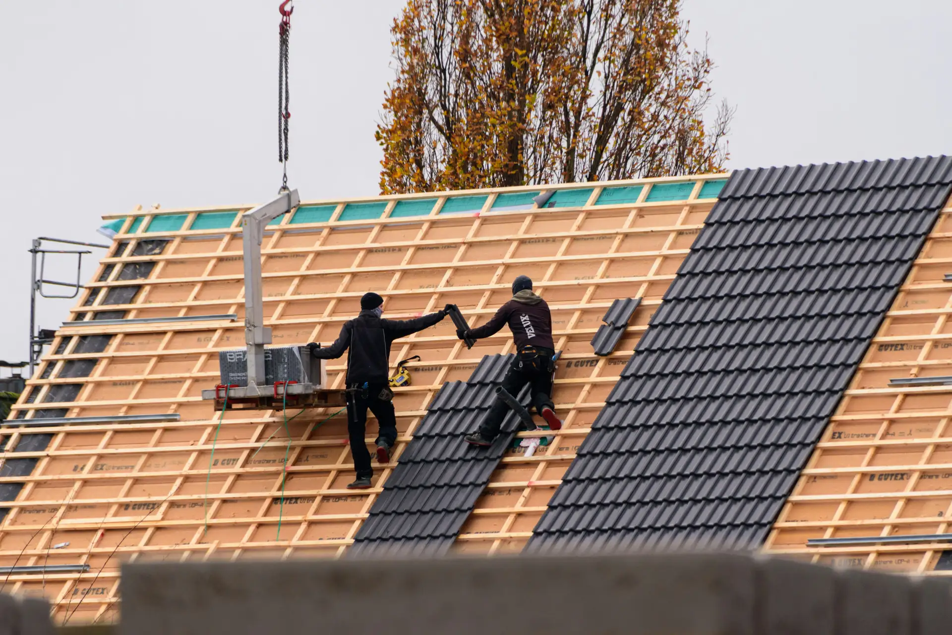 Deux couvreurs posent des tuiles sur une charpente en construction