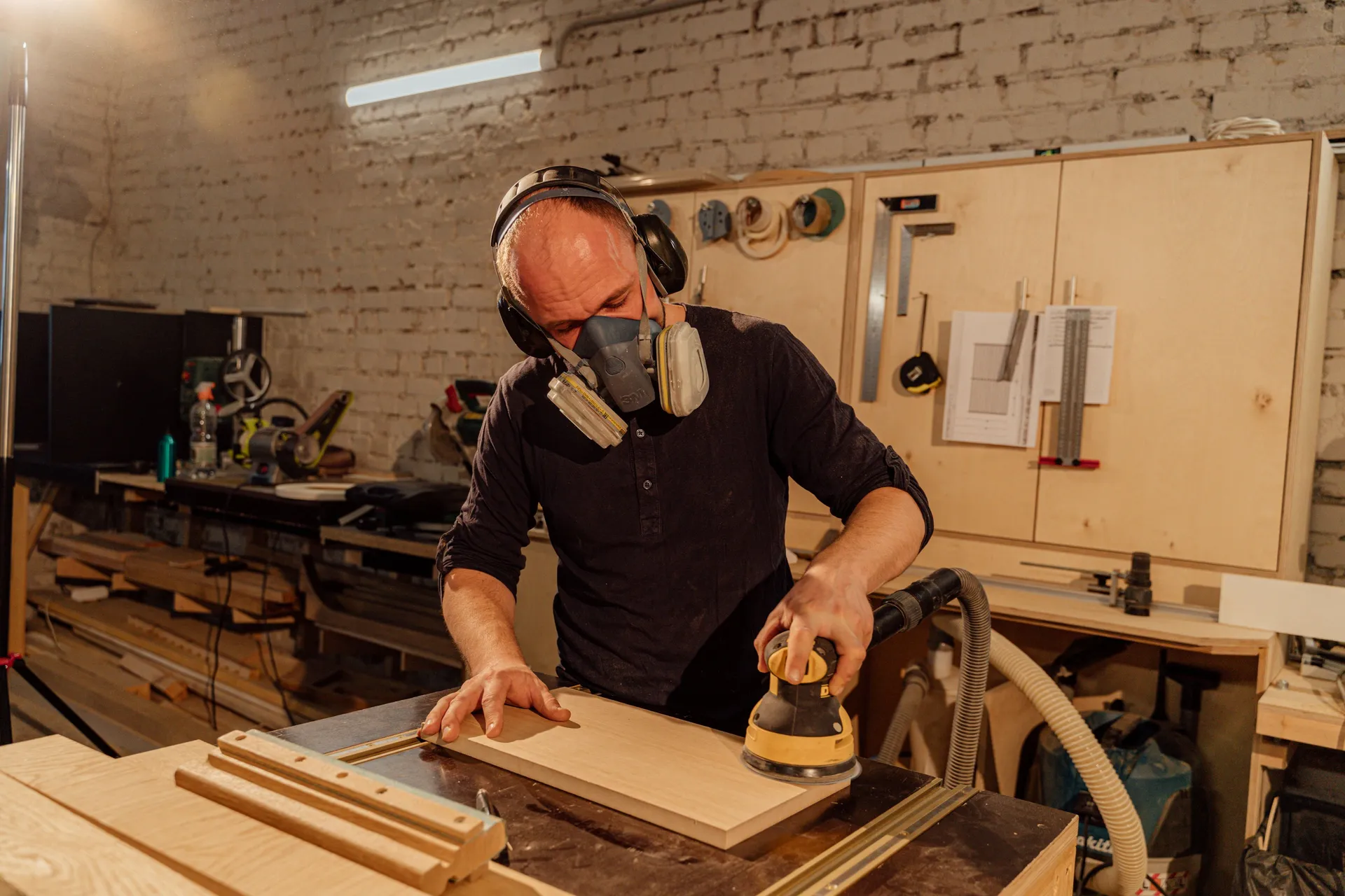 Menuisier au masque de protection ponçant une planche en atelier